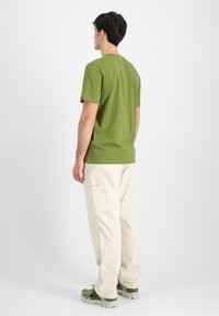 Grøn kortærmet T-shirt lavet af blødt bomuld, parret med cremefarvede cargo-bukser og grå-grønne sneakers. Enkel design, ingen synlige mønstre.