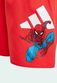 Shorts deportivos rojos con un gráfico de Spider-Man en azul y un logo de Adidas en blanco. Fabricados con una tela suave, presentan acentos de color contrastantes.