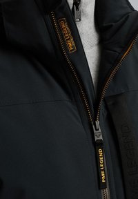 Schwarze Jacke mit Rei�ßverschluss, strukturiertem Stoff und einem orangenen Logolabel. Enthält einen grauen Strickkragen darunter.