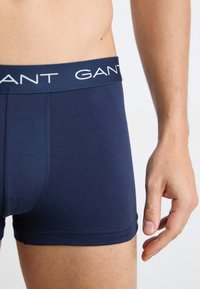 Marineblå boksershorts med en glatt tekstur, med en kontrasterende hvit "GANT"-logo på den elastiske midjebåndet og flate sømmer.