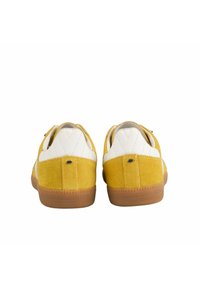 Baskets en daim jaune avec des accents en cuir blanc, une silhouette basse, une semelle en caoutchouc texturé et un logo à l'arrière.