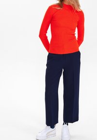 Rotes, geripptes Langarmoberteil kombiniert mit marineblauen weit geschnittenen Hosen und weißen Plattform-Sneakern, mit einem taillierten Schnitt und glatter Textur.