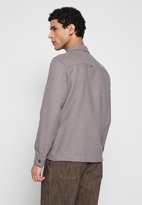 Grijs gestructureerd overhemd met een kraag, manchetten met knopen en een detail van een rugnaad. Draag het met bruin gestreepte broek voor een gelaagde look.