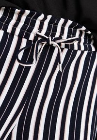 Marinblå och vit randig tyg med ljusrosa detaljer; har en elastisk midja med dragsko och metallspets.