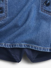 Denimtyg i mörkblått med en slät textur. Har en rundad fåll, synlig orange sömnad och mörka knappar på kragen.