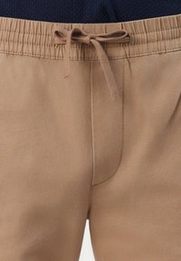 Beige shorts med elastisk linning og snor. Glatt stofftekstur med et enkelt design og diskrete sømdetaljer.