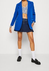 Ljust blå oversized kavaj, grå kort klädd topp, mörk denim utsvängd kjol, vita strumpor och kraftiga svarta loafers. Släta texturer, avslappnad stil.