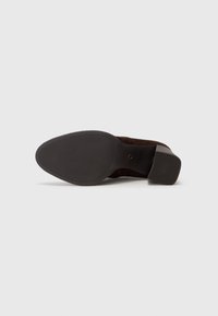 Chaussure à talon en daim marron avec une semelle extérieure en caoutchouc à motif et un bout arrondi. Dotée d'un petit talon carré pour la stabilité et la traction.