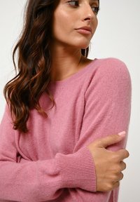 Maglione in cashmere rosa con collo a giro e polsini a coste. Il tessuto appare morbido con una leggera texture pelosa, evidenziando una vestibilità rilassata.