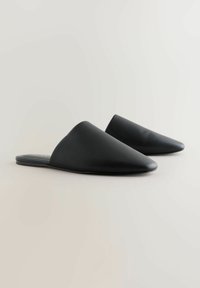 Juodos smailianos nosies mules, su lygiu odiniu viršumi, lengvai užsidėjamomis, plokščiu padu ir švariu, minimalistiniu estetiniu stiliumi.