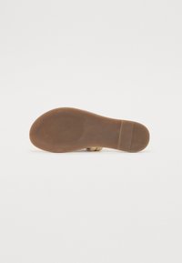 Tan sandal såle med en glatt overflate, lette teksturerte spor og en avrundet kant; har en flat hæl og minimale designelementer.