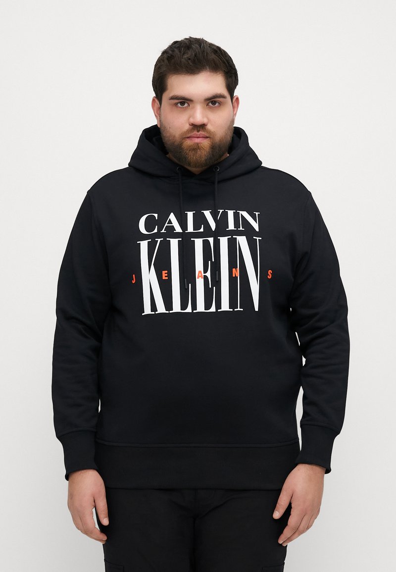 Hanorac negru realizat dintr-un material moale, având un logo mare și îndrăzneț "CALVIN KLEIN JEANS" în alb și portocaliu. Glugă cu șnururi și manșete cu nervuri.