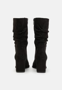 Bottes hautes jusqu'au genou en daim noir avec un design froncé, dotées d'un talon épais et de fermetures éclair latérales pour un maintien sécurisé. Texture lisse sur toute la surface.