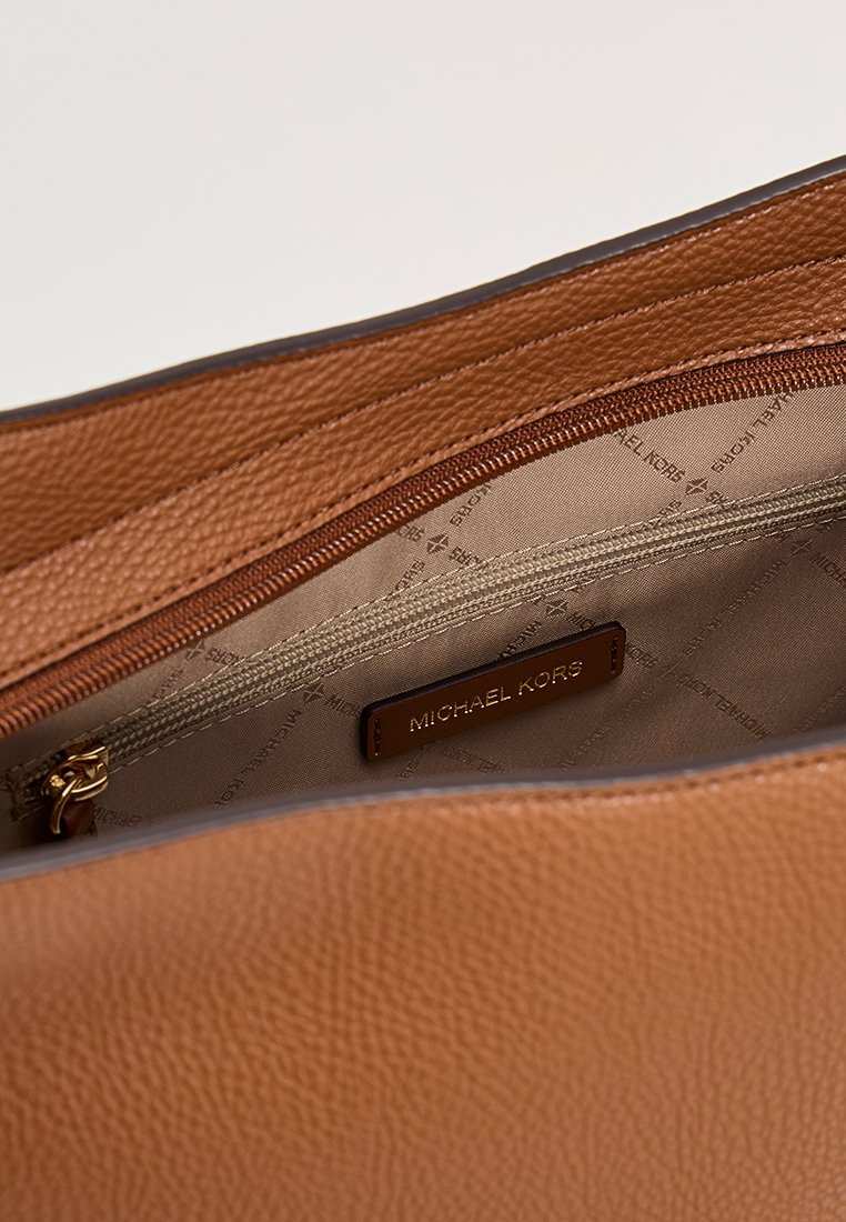 Interior de un bolso de cuero marrón texturizado que muestra un forro de tela beige, un bolsillo con cremallera y una etiqueta de la marca Michael Kors.