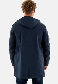 Chaqueta impermeable azul marino con capucha, que presenta un corte recto, costuras laterales y una textura suave y mate. La costura encolada añade detalle.