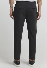 Dark gray trousers made of soft fabric, featuring a straight cut, two back pockets with button closures, and worn with black sneakers.