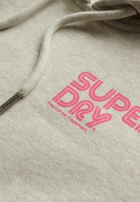 Grijze sweatshirt met een groot, vet, roze logo met de tekst "SUPER DRY." Inclusief een textuur trekkoord en een klein merklabel.