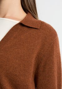 Brązowy kardigan z wełny z dodatkiem innych włókien o miękkiej fakturze, z klasycznym kołnierzykiem i lekko luźnym krojem. Materiał ma subtelny blask.