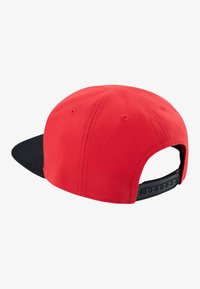 Rød caps med sort br brim, laget av vevet stoff. Har en justerbar snapback-lukking og ventilasjonsøyeblikk bak.