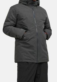 Giacca isolata grigio scuro con cappuccio, cerniera frontale e tasche laterali. Tessuto liscio con finitura opaca e design minimalista.