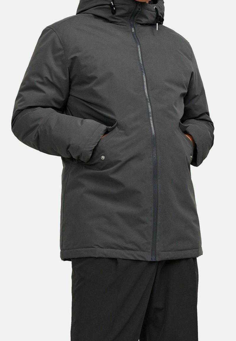 Giacca isolata grigio scuro con cappuccio, cerniera frontale e tasche laterali. Tessuto liscio con finitura opaca e design minimalista.