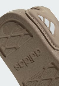 Chancla Adidas deslizante color marrón claro con suela texturizada, logo en relieve y branding blanco de tres rayas en la correa.