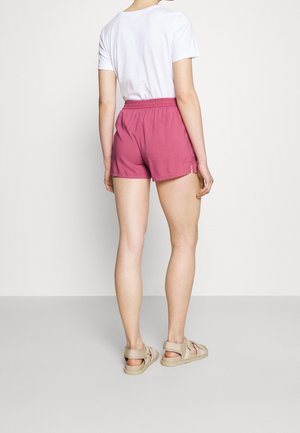 Shorts en coton rose avec taille élastique. Associés à un t-shirt blanc et des sandales beiges. Design minimal et coupe décontractée.