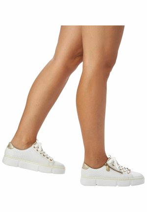 Baskets en mesh blanches avec un accent doré sur le talon, des éléments en métal doré sur le côté et une semelle blanche épaisse avec des détails texturés.