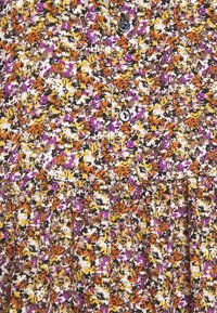 Vêtement boutonné avec taille froncée, présentant un motif floral dense aux couleurs orange, jaune, violet, marron et blanc.