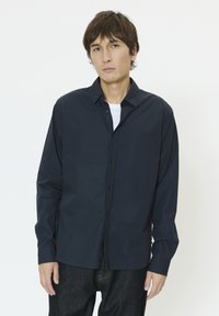 Chemise bleu marine à boutons en mélange de coton, dotée de manches longues, d'un col ouvert et d'une coupe décontractée avec une texture lisse.