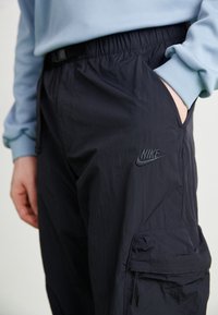 Laivastonsiniset cargo-housut, jotka on valmistettu kevyestä kankaasta. Niissä on joustava vyötärönauha, sivutaskut ja sävy sävyyn oleva Nike-logo reidessä.