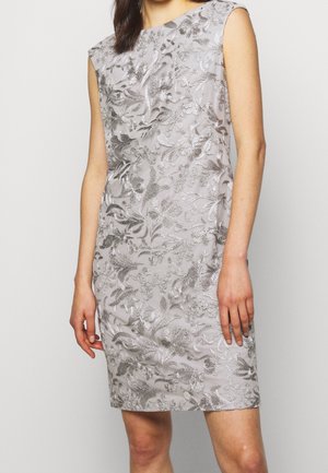 Robe sans manches gris argenté longueur genou avec motif en dentelle florale complexe portée par une personne debout sur un fond uni.