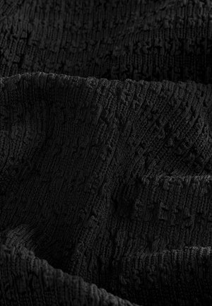 Primer plano de una tela negra texturizada con patrones en relieve en forma de cuadrícula y pliegues suaves e irregulares.