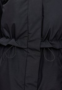 Schwarze gepolsterte Jacke mit tailliertem Schnitt, die über eine glatte Textur, Zugbänder und subtile Steppnähte entlang der Nähte verfügt.