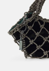 Schwarze Handtasche mit einem Perlen-Mesh-Design, ausgestattet mit einem grünen Innenraum, Kettenakzenten und einem kleinen dekorativen Charme.