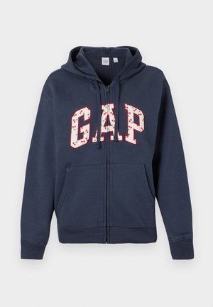 Tumši zils zipa kapuce ar priekšējiem kabatām, kapuci ar aukliņām un "GAP" burtiem, kas izcelti ķiršu rakstā un sarkanā kontūrā uz krūtīm.