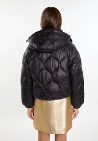 Black puffer jacket with a quilted pattern and hood, featuring a shiny texture. Worn over a metallic gold skirt.