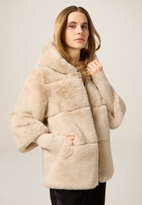 Beżowa kurtka z kapturem z futerka ekologicznego o puszystej fakturze, z prążkowanymi ściągaczami na mankietach i dwoma bocznymi kieszeniami, zaprojektowana z poziomymi przeszyciami.