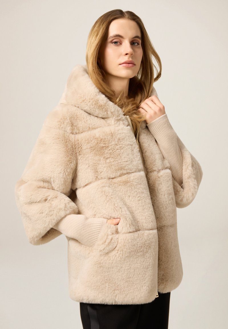 Beżowa kurtka z kapturem z futerka ekologicznego o puszystej fakturze, z prążkowanymi ściągaczami na mankietach i dwoma bocznymi kieszeniami, zaprojektowana z poziomymi przeszyciami.