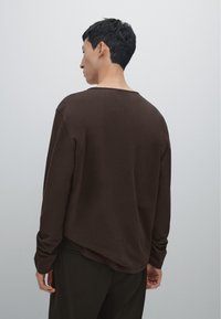 Braunes Langarmshirt mit Rundhalsausschnitt und lockerer Passform, mit glatter Textur und gewelltem Saum. Ideal für die Freizeit.