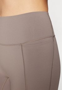 Høy midje leggings i en dempet brun tone, med en jevn tekstur, flate sømmer og et enkelt design uten mønstre eller dekorasjoner.