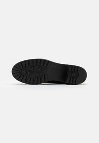 Semelle de chaussure en caoutchouc noir avec un motif de bande de roulement profond, incluant des accents triangulaires et des rainures horizontales pour une adhérence optimale. Design plat et robuste.