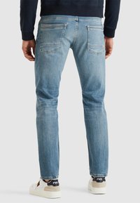 Ljusblå denimjeans med slim fit, bakfickor, subtil blekning och enkel söm, bärs med vita och beige sneakers.