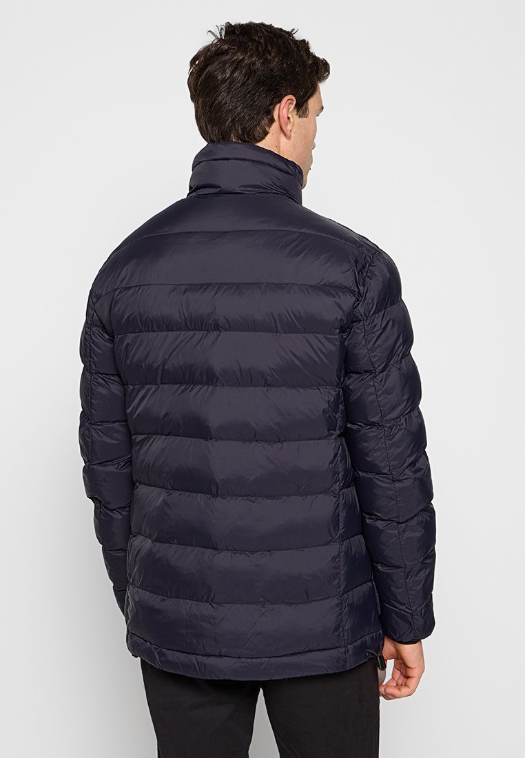 Marineblauwe pufferjack met horizontaal gequiltte panelen, hoge kraag en een gladde, glanzende stofstructuur. Geen zichtbare hardware of logo's.