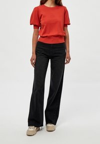 Punainen ribbineulotusta lyhythihainen paita yhdistettynä korkeavyötäröisiin mustiin leveälahkeisiin farkkuihin, beigejen tennareiden kera. Yksinkertainen, rento asu.