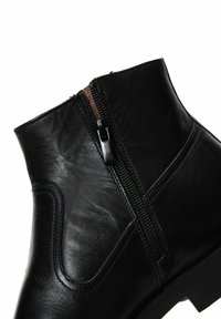 Botín negro de cuero hasta el tobillo con cremallera lateral, textura suave, diseño ligeramente curvado y costuras reforzadas a lo largo de los bordes.