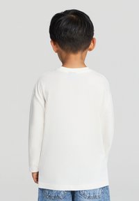 Biała koszulka z długim rękawem, wykonana z bawełny, z okrągłym dekoltem i prostym krojem, noszona z niebieskimi dżinsami.