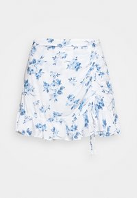 Blommig kjol med vit botten och blå rosor, rynkade sidor och fransad nederkant. Tillverkad av lättviktig tyg.