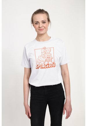 Vrouw draagt wit T-shirt met oranje SpongeBob en Gary cartoonontwerp, gecombineerd met zwarte broek, staand tegen een effen achtergrond.