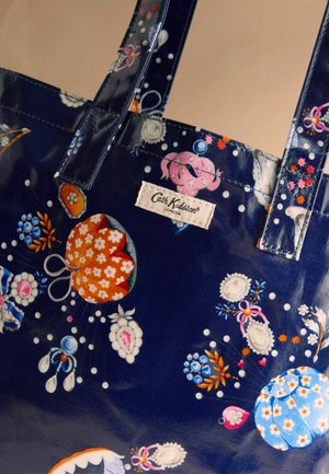 Granatowa torba na ramię z kwiatowym wzorem w kolorach pomarańczowym, niebieskim, białym i różowym, z przeszywanymi uchwytami i materiałową metką "Cath Kidston London".